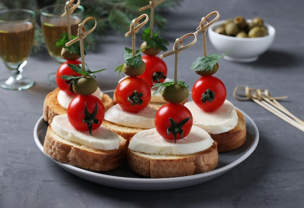 Canapés de mozzarella, tomates cherry, aceitunas verdes, perejil sobre crutones de pan blanco sobre fondo gris oscuro