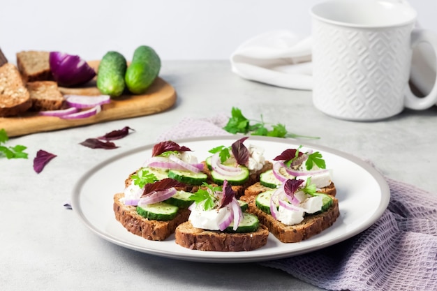 Canapés con pan tostado con semillas de girasol y lino, queso feta, pepino y cebolla