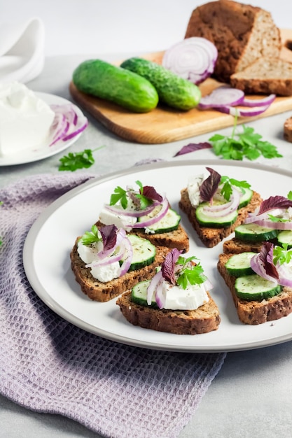 Canapés con pan tostado con semillas de girasol y lino, queso feta, pepino y cebolla