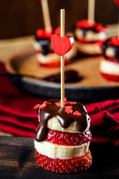 Canapés de plátano y fresa en glaseado de chocolate de cerca, un aperitivo original para San Valentín. Foto de alta calidad