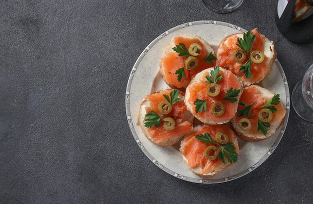 Canapés de salmón salado, aceitunas verdes y perejil sobre picatostes de pan blanco sobre fondo gris oscuro Aperitivo festivo