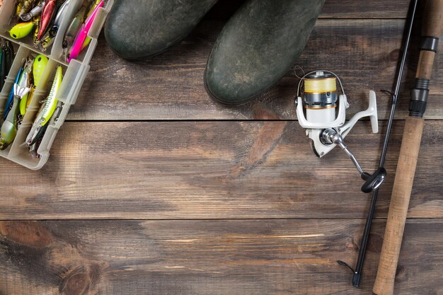 Cañas de pescar y carrete con botas y aparejos de pesca en una caja sobre fondo de madera