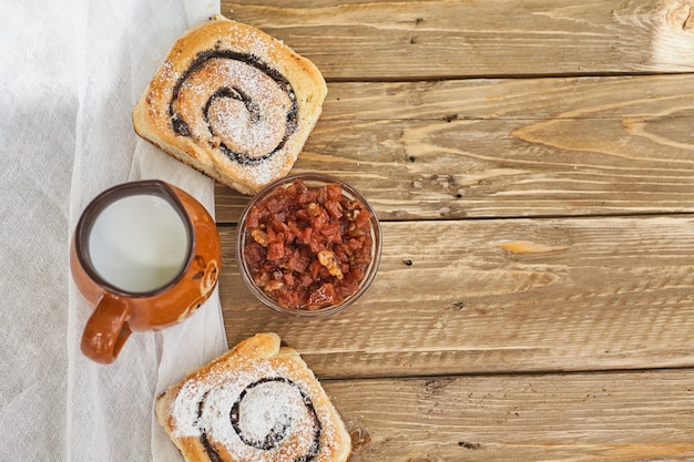 Canasta de bollos caseros con mermelada, servido en una mesa de madera vieja con una taza de leche