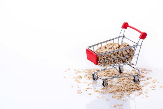 Una canasta de carrito de supermercado de avena con copos de avena sobre un fondo blanco Alimentos saludables