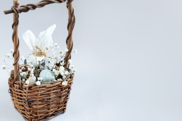 Canasta de mimbre de Pascua llena de pequeños huevos manchados decorados con flores blancas sobre superficie clara.