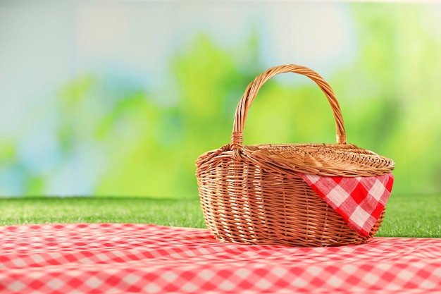 Una canasta de mimbre de picnic con servilleta a cuadros y una manta en la hierba contra un fondo verde borroso Espacio para el texto