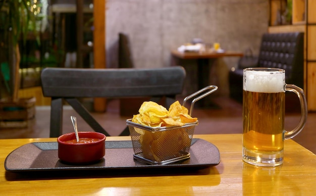 Una canasta de papas fritas y un chapuzón con un vaso de cerveza fría en la mesa de madera