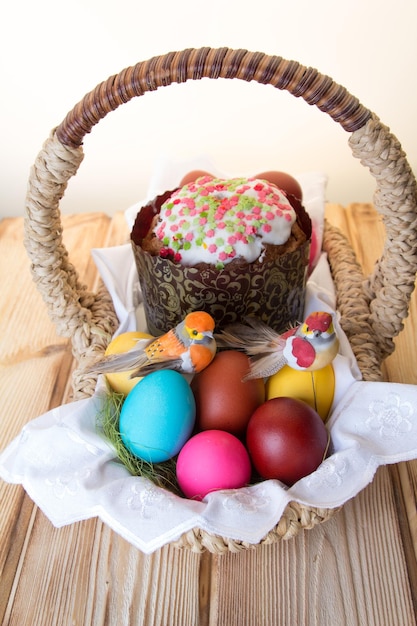 Una canasta de Pascua con un pájaro de juguete sentado sobre huevos de colores brillantes y un pastel