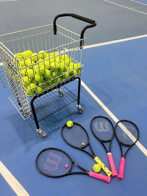 Una canasta de pelotas de tenis está en un piso azul con una canasta llena de pelotas de tenis.