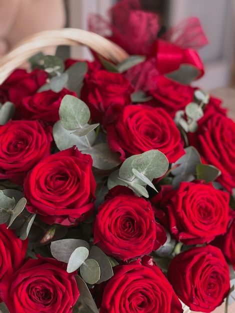 Una canasta con rosas rojas brillantes y eucalipto en una silla en una florería. Un hermoso ramo de flores para las vacaciones. Fondo para la postal