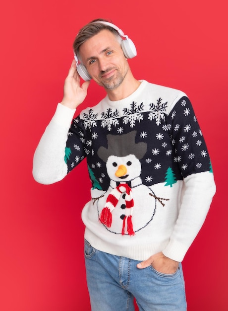 Foto canções de natal homem com fone de ouvido retrato de estúdio de cara usa chapéu de papai noel e suéter de inverno homem com chapéu de natal sobre fundo vermelho isolado