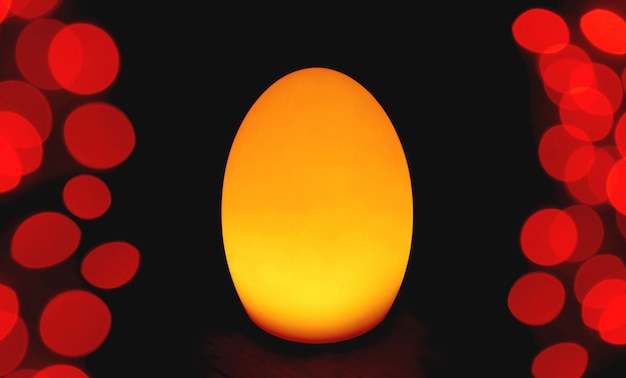 Candeeiro de mesa em forma de ovo amarelo dourado brilhante com luz vermelha Bokeh sobre fundo escuro