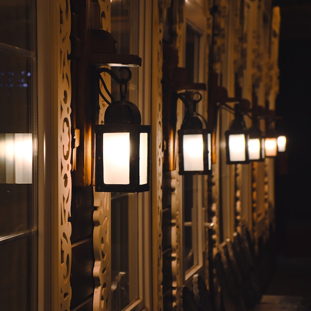 Candeeiros de parede vintage iluminam-se numa linha na casa de madeira Fachada da casa de madeira