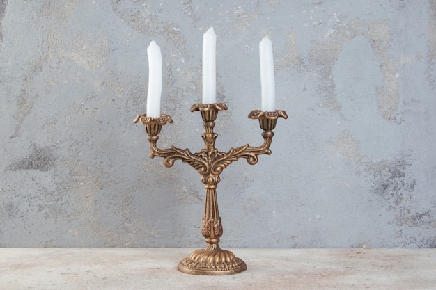 Candelabro de latón antiguo para tres velas sobre fondo de hormigón. Copie el espacio para el texto.