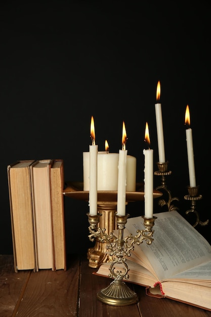 Candelabros retro con velas y libros sobre mesa de madera sobre fondo negro