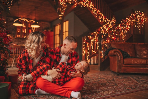 Candid auténtica linda familia feliz en pijama de cuadros rojos pasa tiempo juntos en el albergue decorado con Navidad