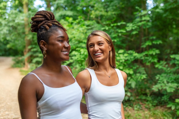 Candid dos mujeres diversas caminando juntas afuera riendo y sonriendo