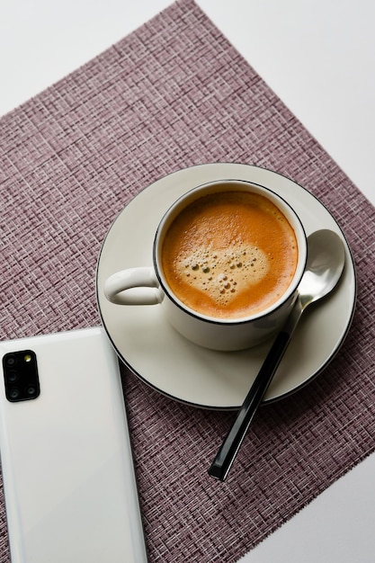 caneca branca com café, rosquinha e um telefone em um fundo roxo. vista do topo. café da manhã