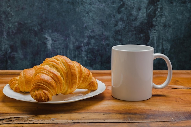 Caneca branca e croissants na mesa de madeira Maquete de caneca em branco