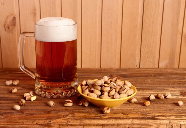 Caneca com cerveja light e pistache na mesa de madeira