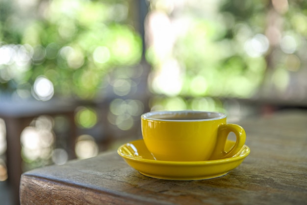 Caneca de café amarela na tabela de madeira com o fundo borrado.