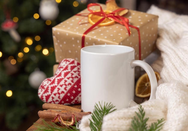 Caneca de café branca perto de presente de Natal, coração aconchegante e maquete de inverno de suéter