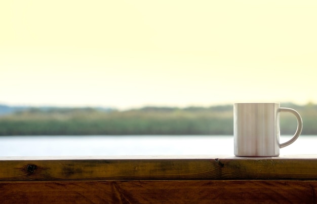 Caneca de café no terraço de madeira com vista para o rio em dia ensolarado