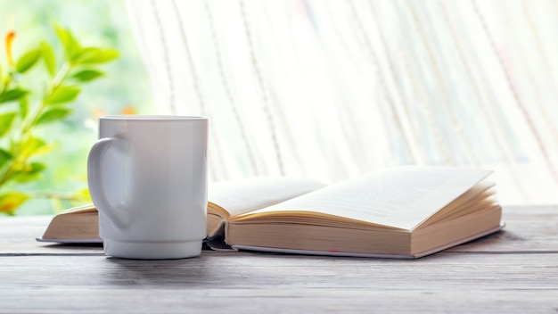 Caneca de café perto de um livro aberto e vaso de flores