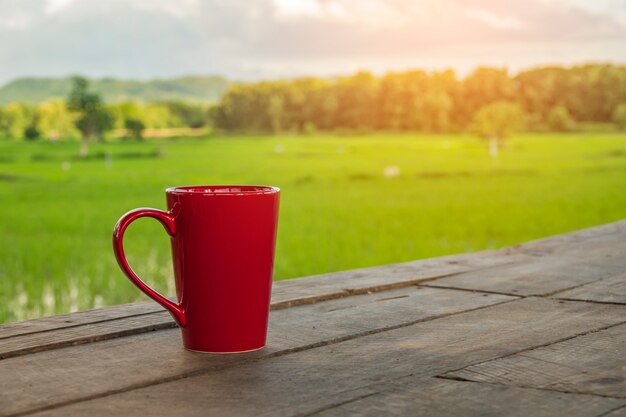 Caneca de café vermelha repousa na varanda com belos campos de arroz.