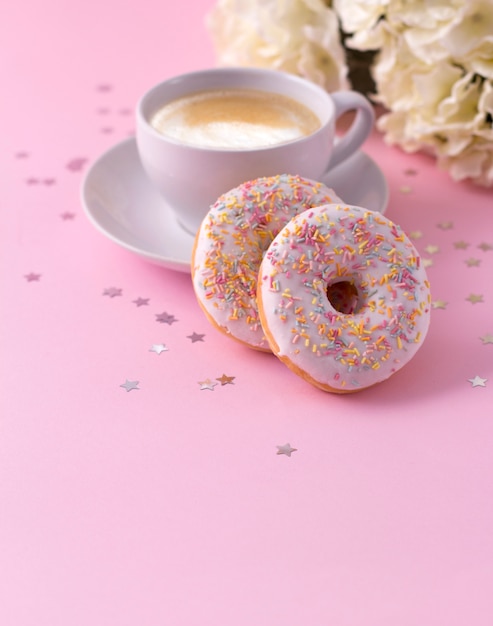 Caneca de cappuccino quente e dois donuts com flores em rosa