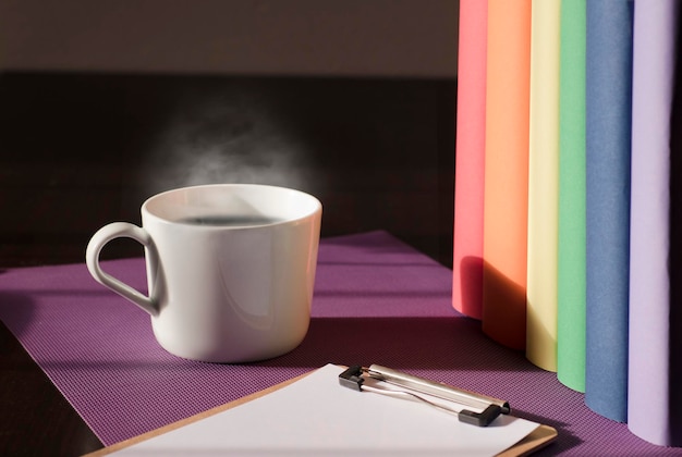 Caneca de cerâmica branca com café quente em fones de ouvido de mesa de trabalho roxos e livros com cor de movimento lgbt