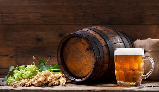 Caneca de cerveja com lúpulo verde e espigas de trigo na mesa de madeira