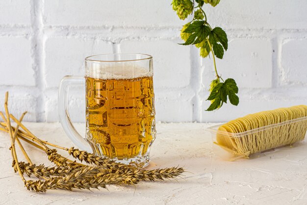 Caneca de cerveja de vidro com batata frita, espigas de cevada e um galho de lúpulo na superfície branca