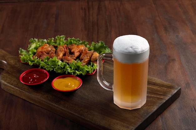 Caneca de cerveja na tábua de madeira com porção de frango frito