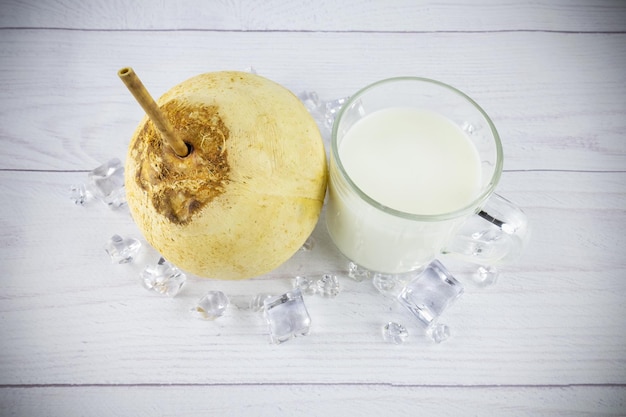 Caneca de coco e vidro com leite e cubos de gelo na mesa branca vista de cima