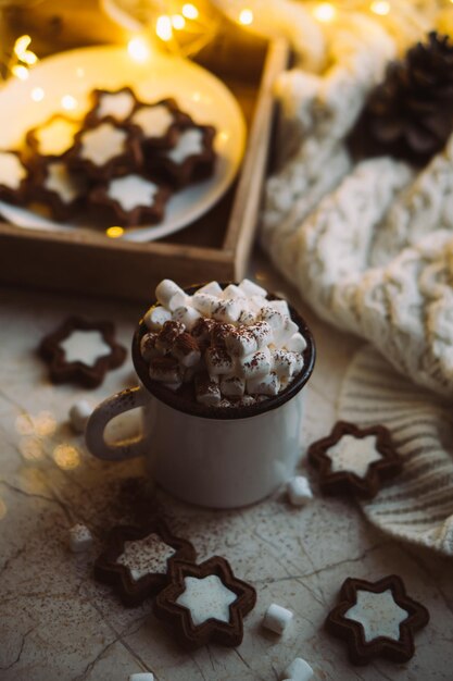 Caneca de comida de Natal reconfortante de cacau quente com marshmallow e biscoitos com luzes aconchegantes