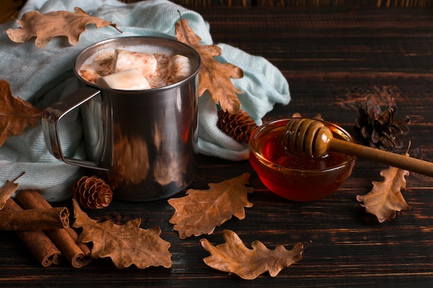 Foto caneca de ferro com cacau, mel, marshmallows, especiarias, sobre um fundo de um cachecol, folhas secas em uma mesa de madeira. clima de outono, uma bebida quente. copyspace.