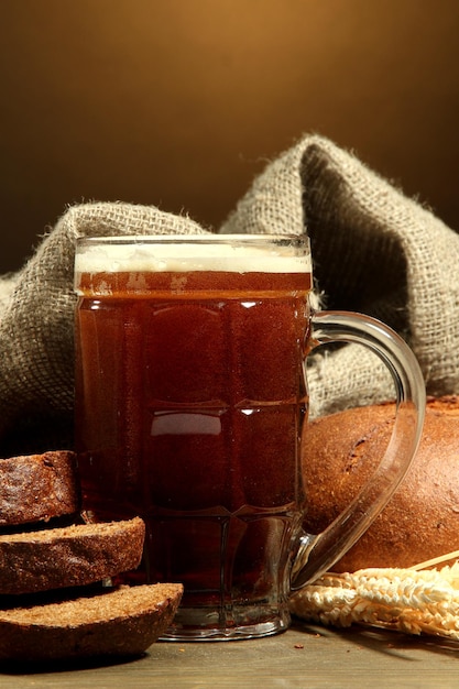 Caneca de kvass e pães de centeio com orelhas na mesa de madeira no fundo marrom