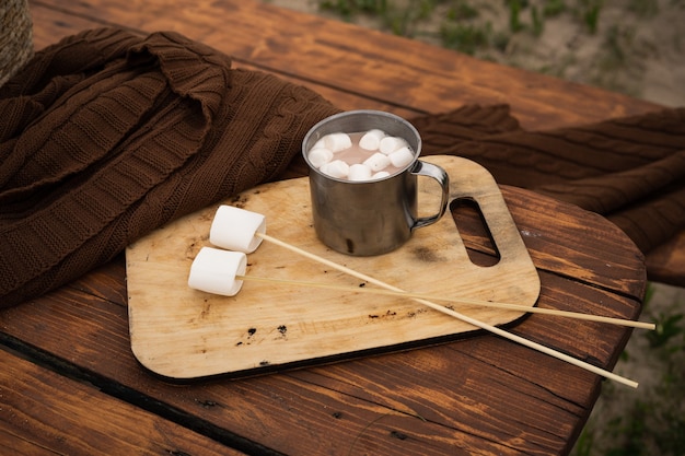 caneca de lata de viagem com chocolate e marshmallows em palitos na tábua de madeira