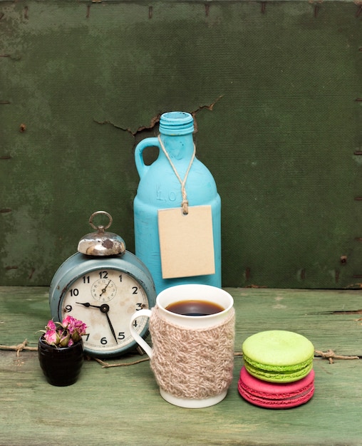 Caneca de malha, biscoitos, garrafa azul e relógio no grunge verde