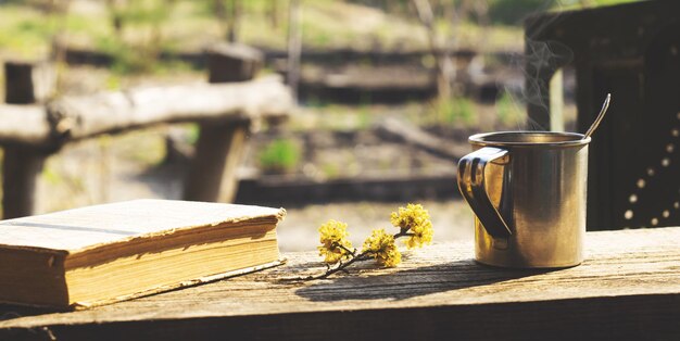 Foto caneca de metal, galho de flor e um livro sobre uma mesa de madeira no jardim