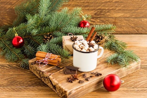 Caneca esmaltada branca com chocolate quente ou cacau, pedaços de chocolate e canela em pau sobre uma placa de madeira. o conceito de um Natal aconchegante.