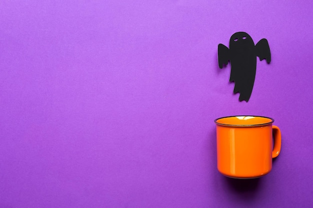 Caneca laranja em um fundo roxo com terríveis decorações de Halloween O conceito do feriado de Halloween Beba festa divertida Copie o espaço simulado lisamente