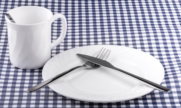 Caneca vazia com prato de colher com faca e garfo na toalha de mesa em uma gaiola vista de cima com...