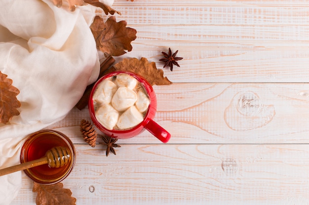 Caneca vermelha com cacau e marshmallows, sobre um fundo de um cachecol e folhas secas. clima de outono, uma bebida quente.