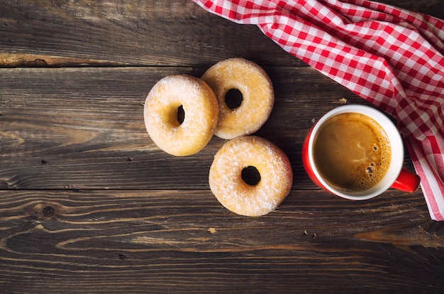 Caneca vermelha com café e donuts em fundo de madeira rústico. vista do topo.