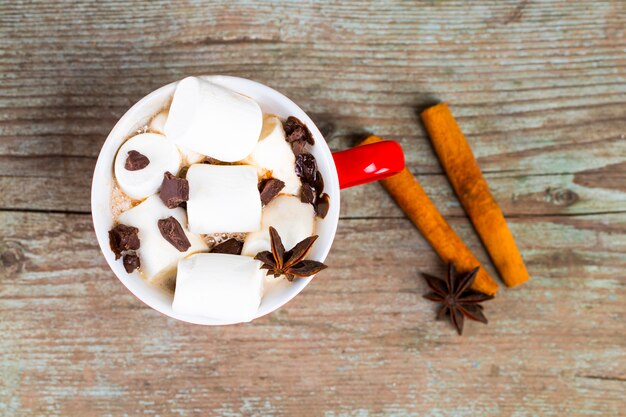 Caneca vermelha com chocolate quente com canela derretida de marshmallow e anis estrelado em fundo de madeira a vista de cima