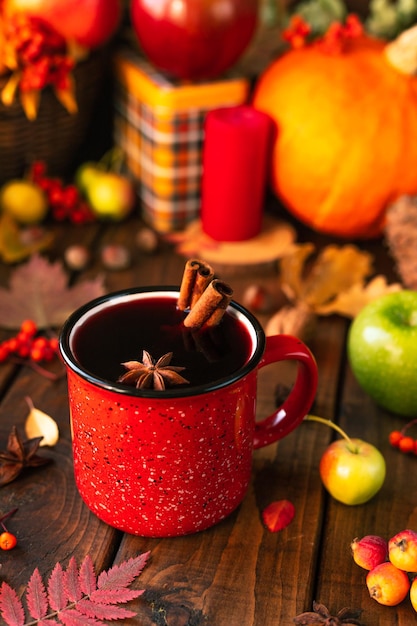 Caneca vermelha com vinho quente. Paus de canela saem do copo e uma estrela de anis estrelado flutua. Frutas e especiarias estão por toda parte em uma mesa de madeira