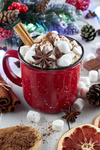 Caneca vermelha de chocolate quente com marshmallow, anis e canela polvilhada com cacau em pó sobre uma mesa de madeira