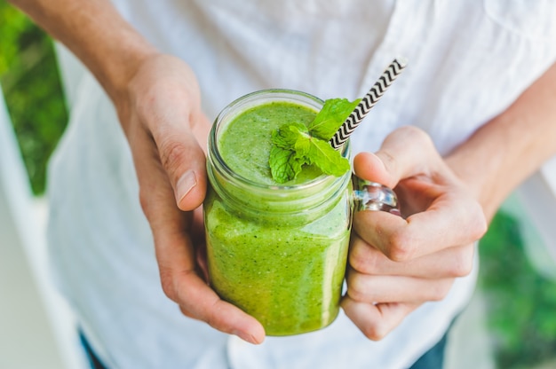 Canecas em frasco de vidro com espinafre verde, banana e vitamina de leite de coco com uma colher de aveia